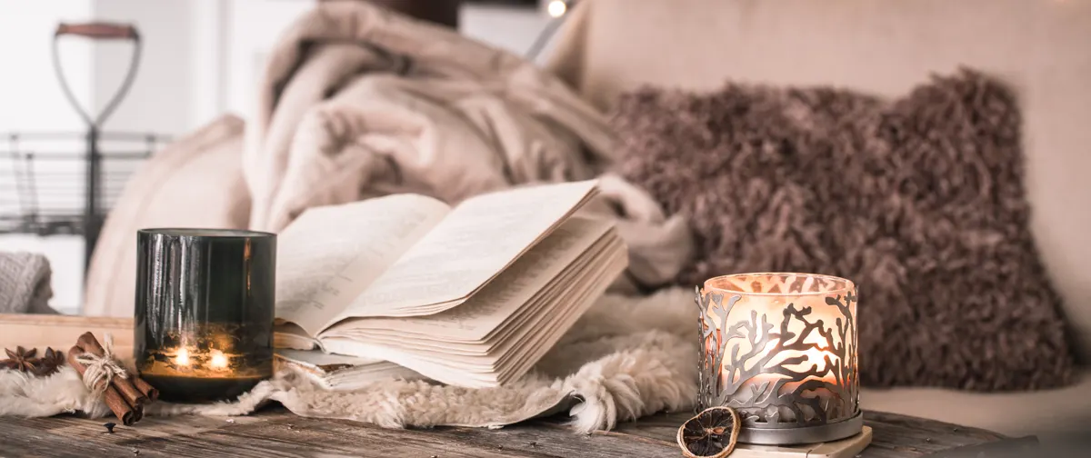 Livro aberto sobre manta com velas acesas, em um ambiente aconchegante